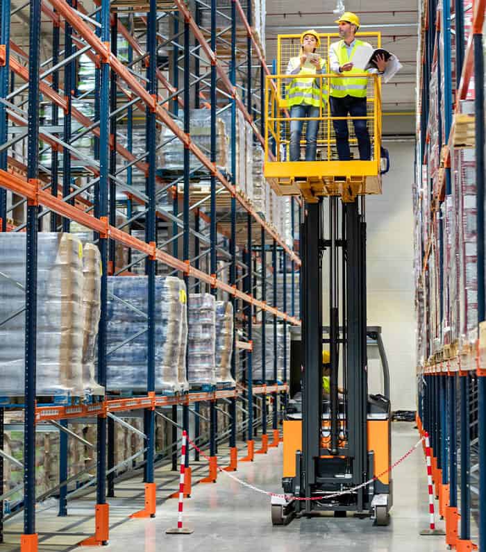 Forklift operator loading pallets of boxed goods into a semi-truck trailer at a warehouse loading dock, demonstrating efficient logistics operations.